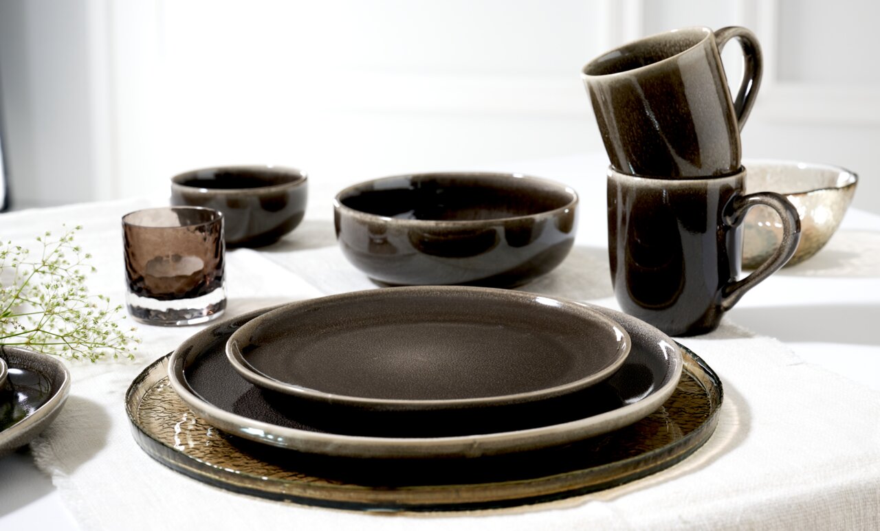 Ritzenhoff & Breker Dessertteller EDA UMBRA Verschiedene Geschirrteile aus der Ritzenhoff & Breker EDA UMBRA Serie, darunter Tassen, Schalen und Teller, in einer eleganten dunklen Farbgebung, auf einem Tisch arrangiert. Perspektive von schräg oben.