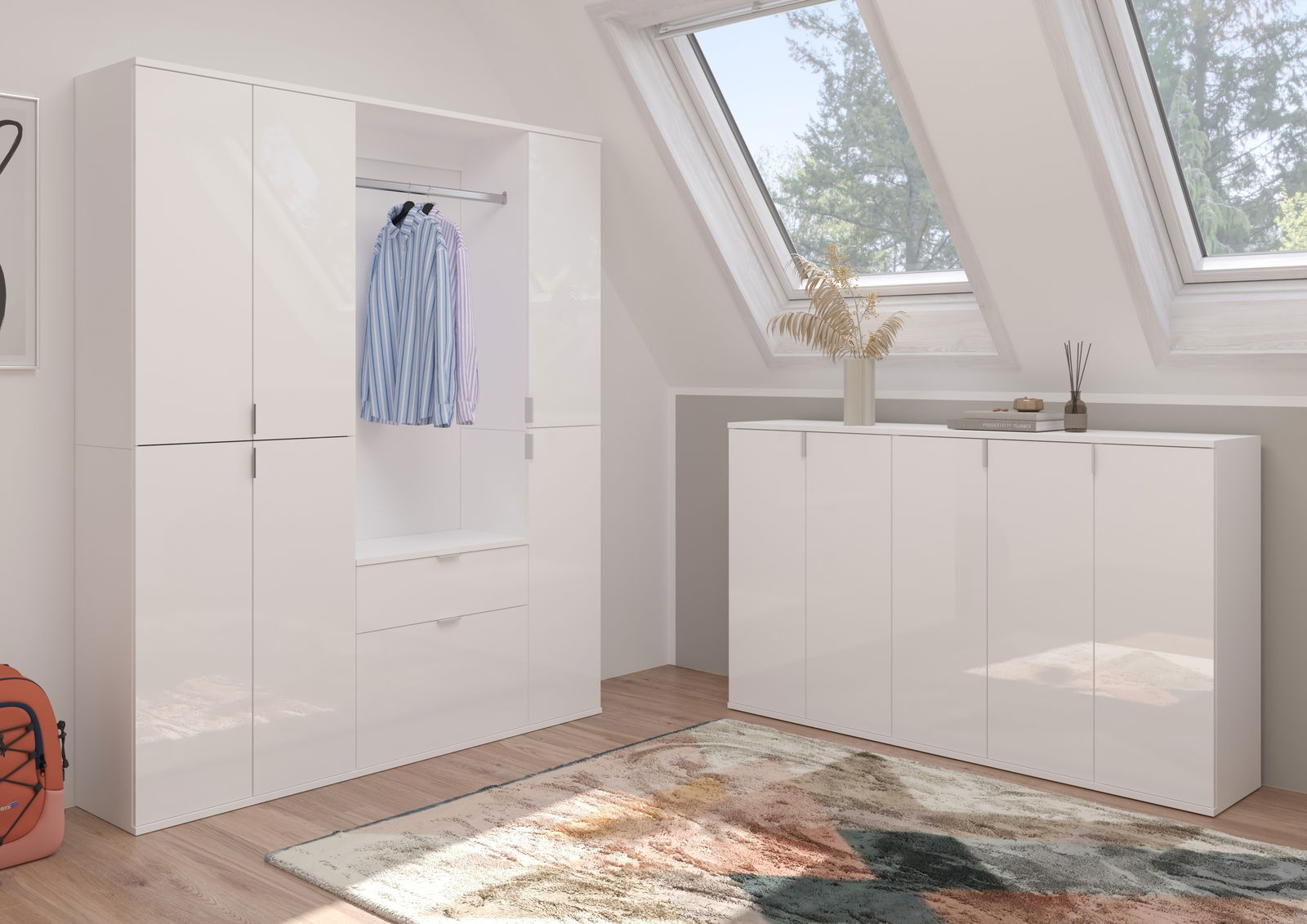 Moderne Garderobenkombination in Weiß mit Hochglanzoberfläche, bestehend aus einem großen Schrank mit Kleiderstange und Schubladen sowie einem Sideboard, in einem hellen Raum mit Dachfenstern, aus seitlicher Perspektive.