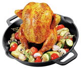 Gusseiserner Hähnchenbräter mit einem goldbraun gebratenen Hähnchen, umgeben von frischem Gemüse wie Zucchini, Tomaten und Pilzen, aus der Vogelperspektive.