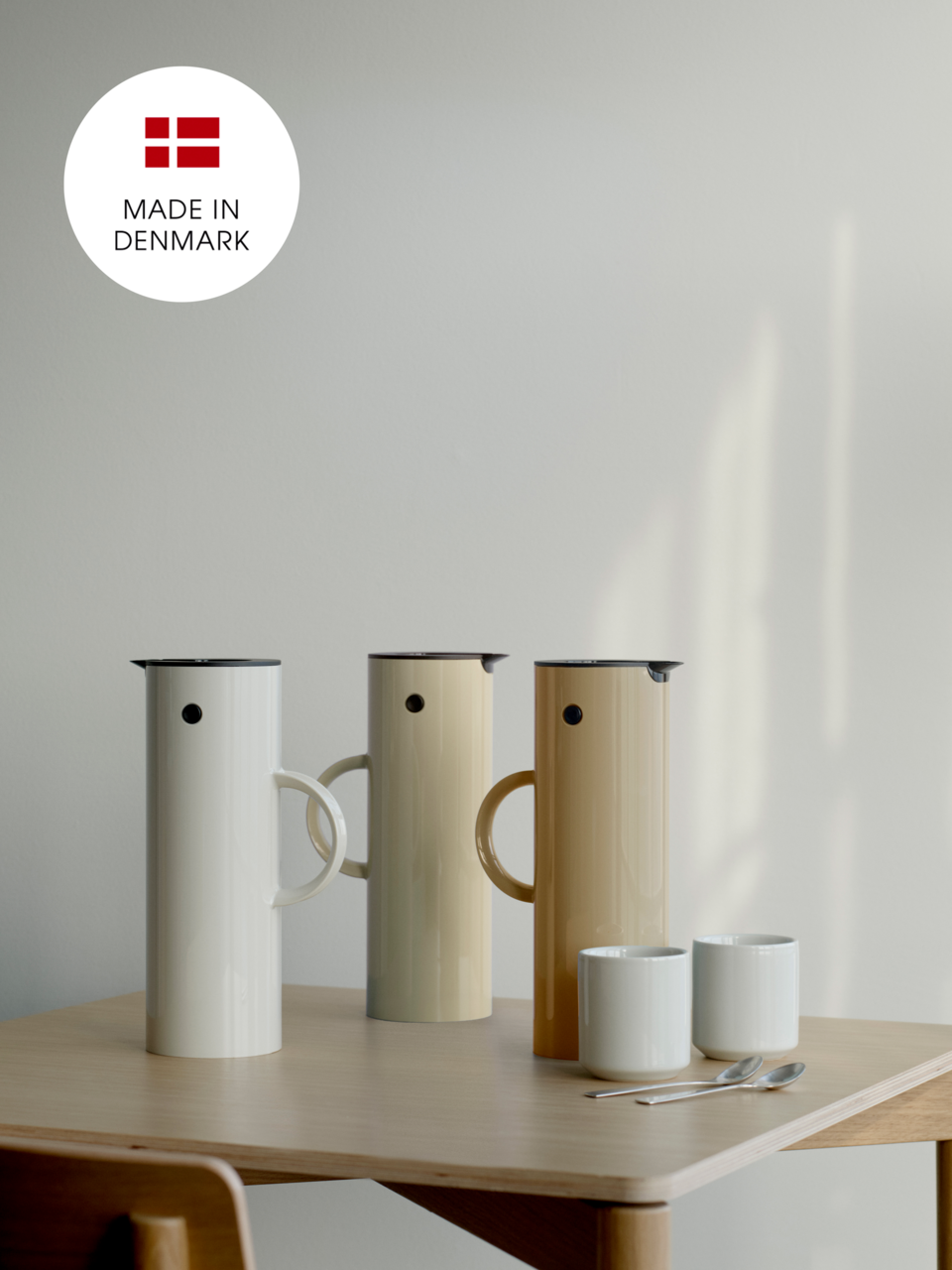 Drei Isolierkannen in verschiedenen Farben auf einem Tisch, mit der Aufschrift 'Made in Denmark' im Hintergrund. Perspektive von vorne.