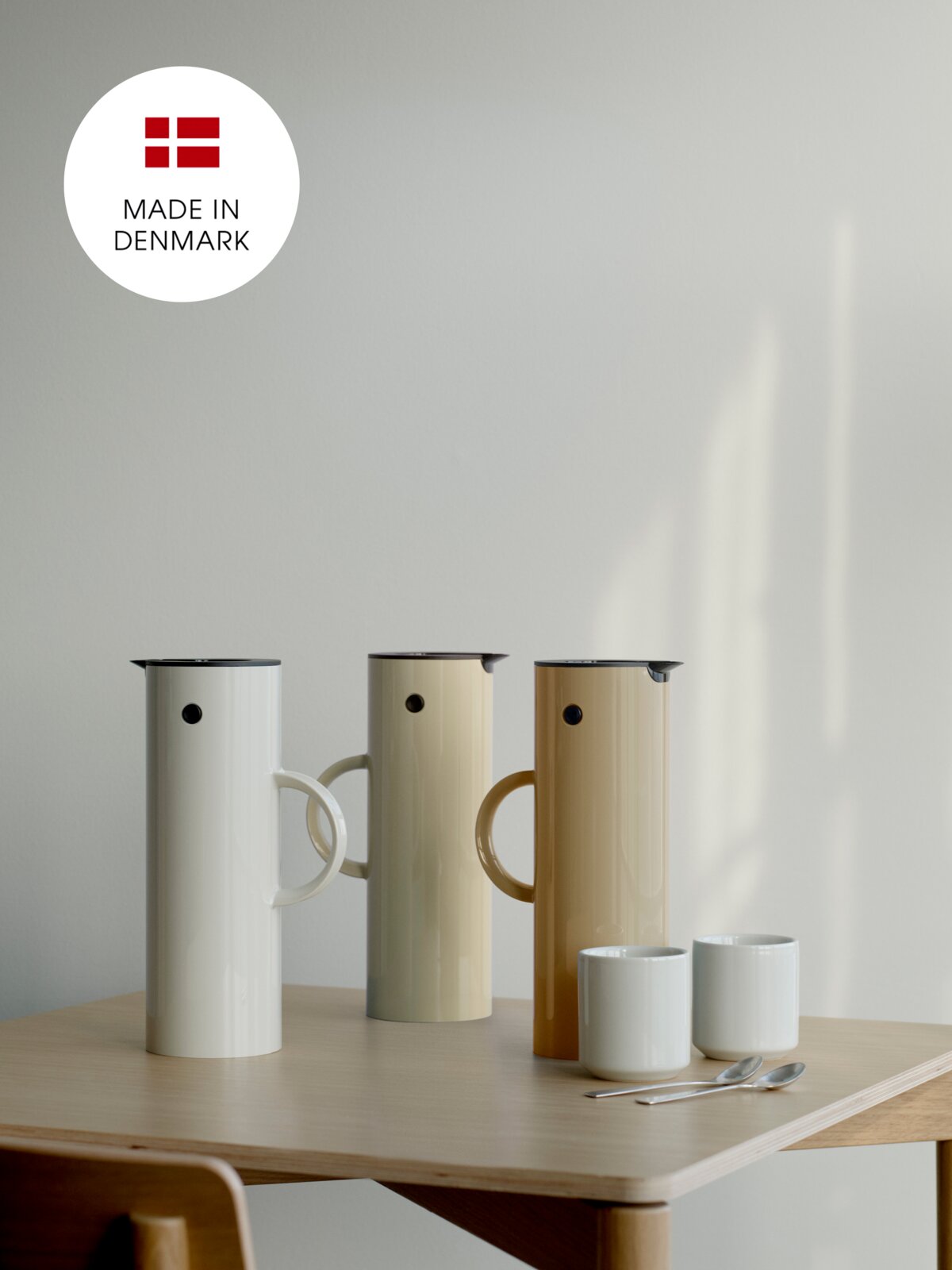 Drie thermoskannen in verschillende kleuren op een tafel, met op de achtergrond het opschrift 'Made in Denmark'. Vooraanzicht.