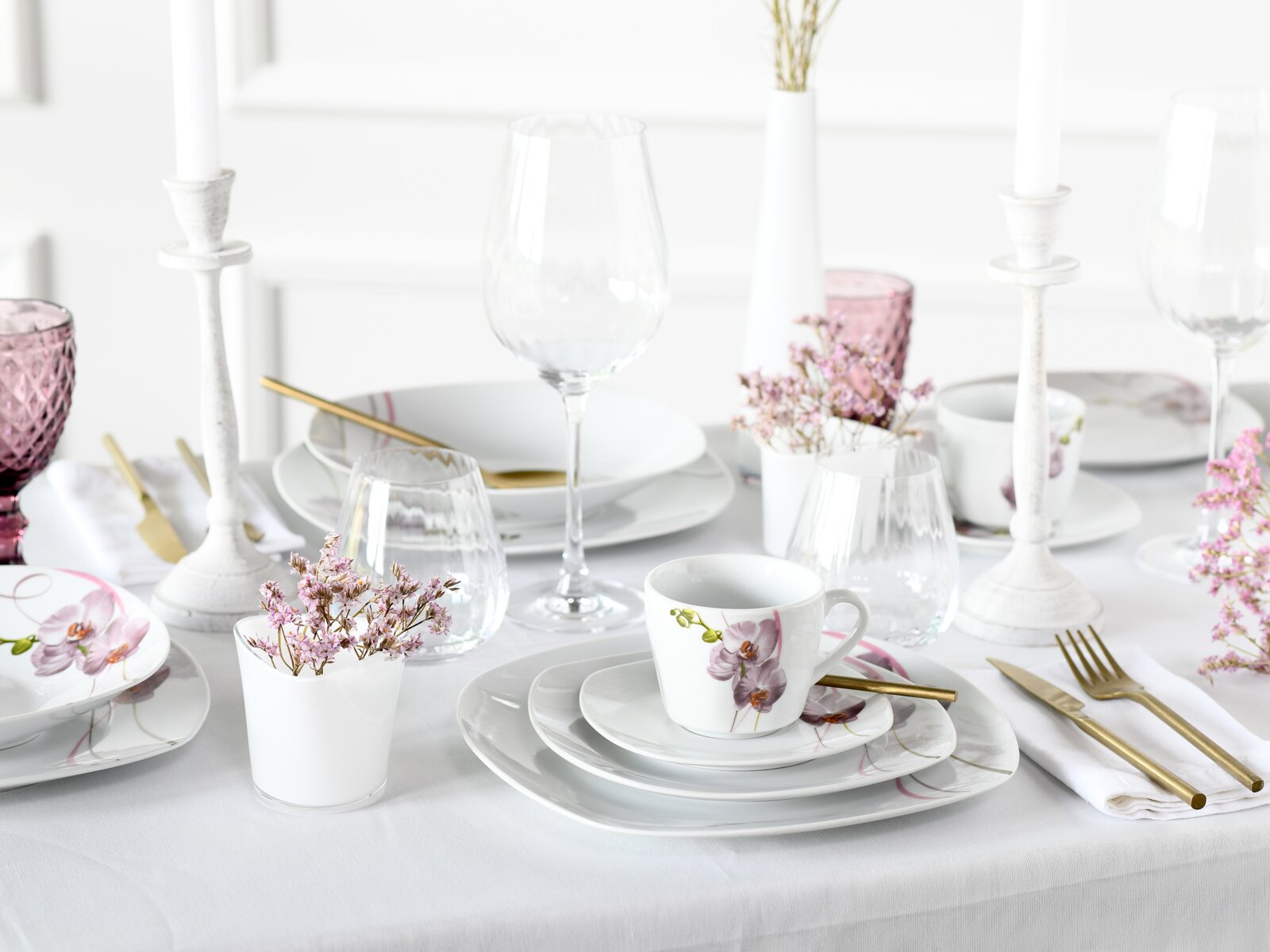 Creatable Kombiservice 62-tlg SQUARE Elegantes weißes Porzellan-Gedeck mit Orchideenmotiv auf gedecktem Tisch, mit Gläsern, Kerzenständern und goldfarbenem Besteck, frontal aus leicht erhöhter Perspektive fotografiert