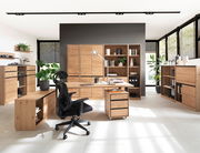 Moderne Büromöbelkombination aus Holz mit Schreibtisch, Rollcontainer und Regalen in einem hellen Raum, seitliche Perspektive.