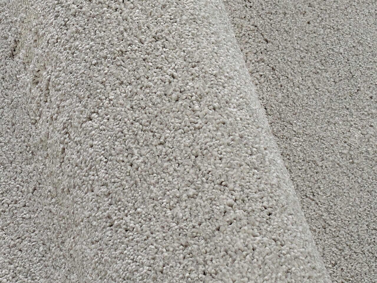 Nahaufnahme eines hellgrauen Uni-Teppichs mit weicher, flauschiger Textur, seitliche Perspektive