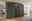 Moderner, sechstüriger Drehtürenschrank in dunklem Design, frontal fotografiert in einem hellen Schlafzimmer.