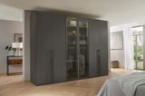 Moderner, sechstüriger Drehtürenschrank in dunklem Design, frontal fotografiert in einem hellen Schlafzimmer.