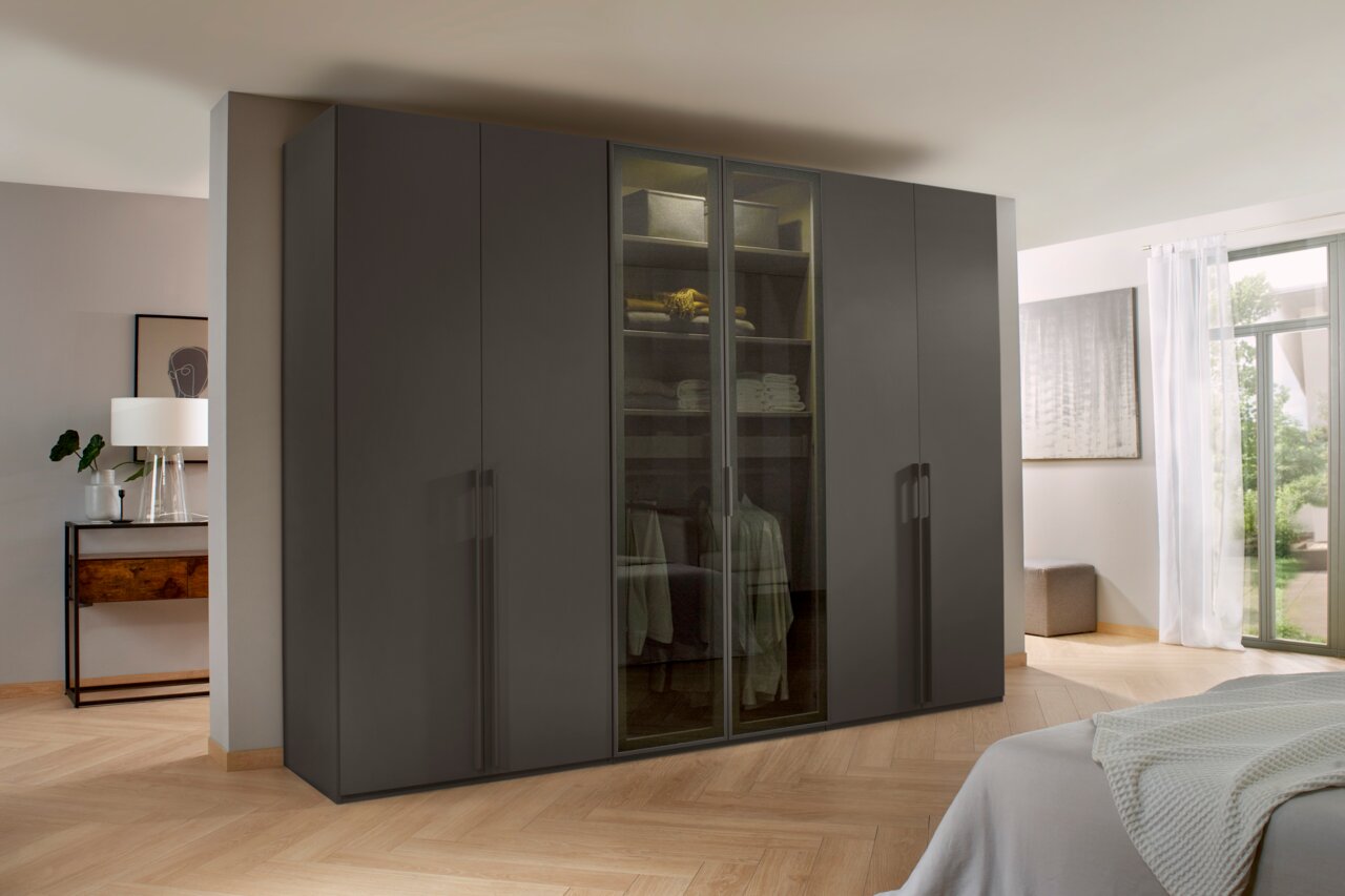 Moderne kast met zes draaideuren in een donkere uitvoering, gefotografeerd van voren in een lichte slaapkamer.