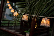Nahaufnahme einer Girlande mit leuchtenden Laternen unter Palmenblättern, seitliche Perspektive