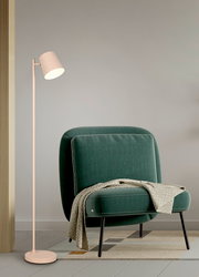 Moderne Akku-Stehleuchte in hellem Beige, neben einem grünen Sessel mit Decke, seitliche Perspektive.