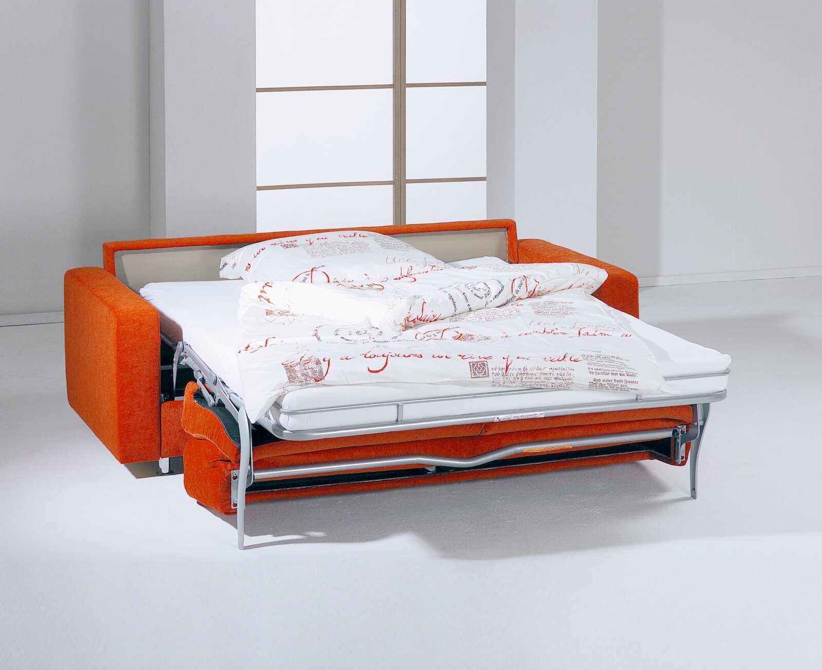 Orangefarbenes Schlafsofa mit ausgeklapptem Metallgestell, Matratze und weißer Bettwäsche mit rotem Schriftmuster, aus schräger Vorderansicht