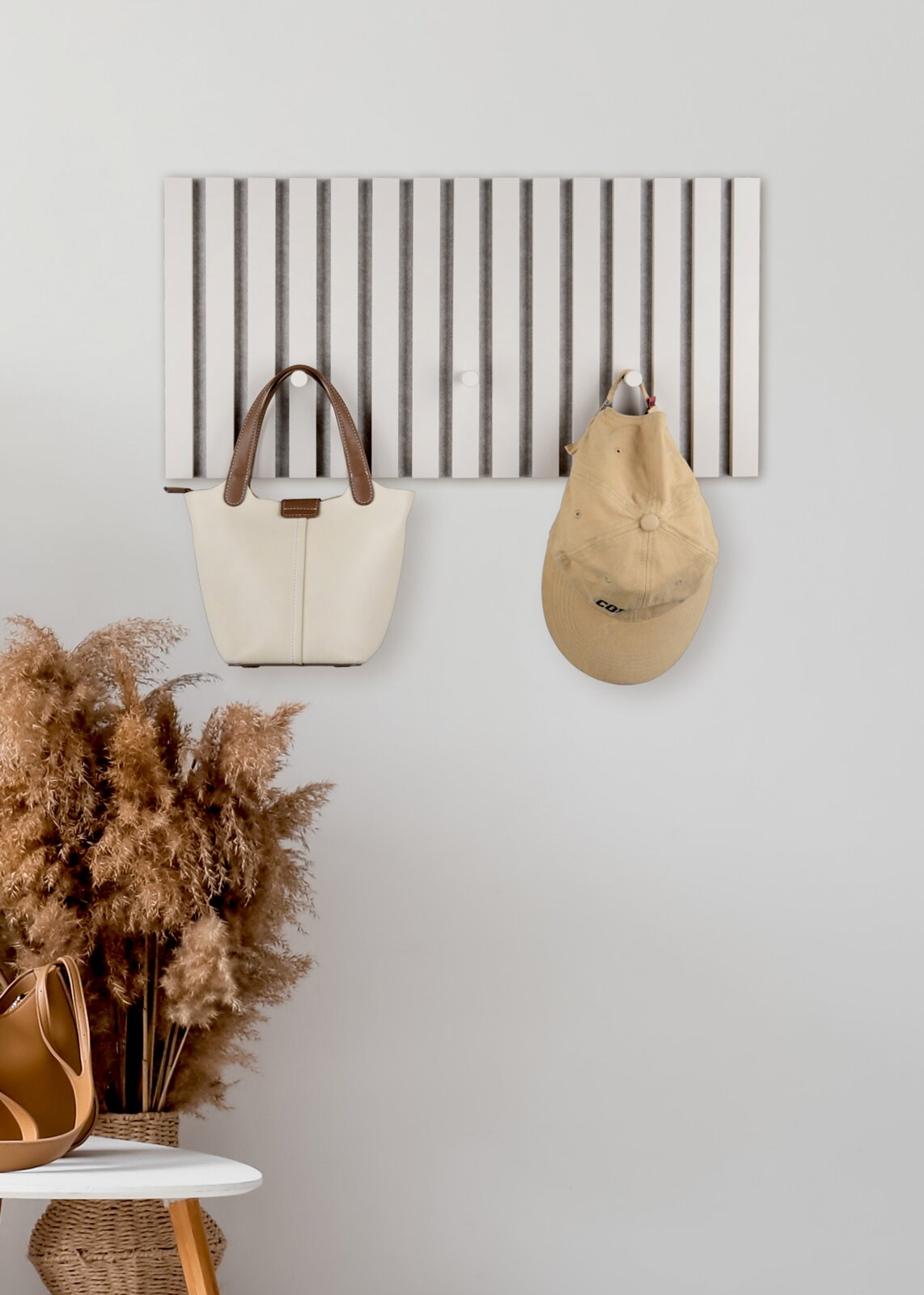 XORA Kapstok GRACE Minimalistische witte wandkapstok/paneel met verticale lamellen en twee haken, waaraan een crèmekleurige handtas en een beige baseballpet hangen, vooraanzicht.