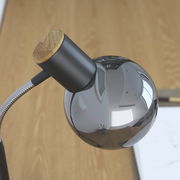 Moderne Tischleuchte mit glänzendem, kugelförmigem Lampenschirm und Holzdetail, aus der Vogelperspektive fotografiert.