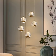 Moderne LED-Hängeleuchte mit fünf kugelförmigen, goldenen und gläsernen Lampenschirmen, von der Seite betrachtet.