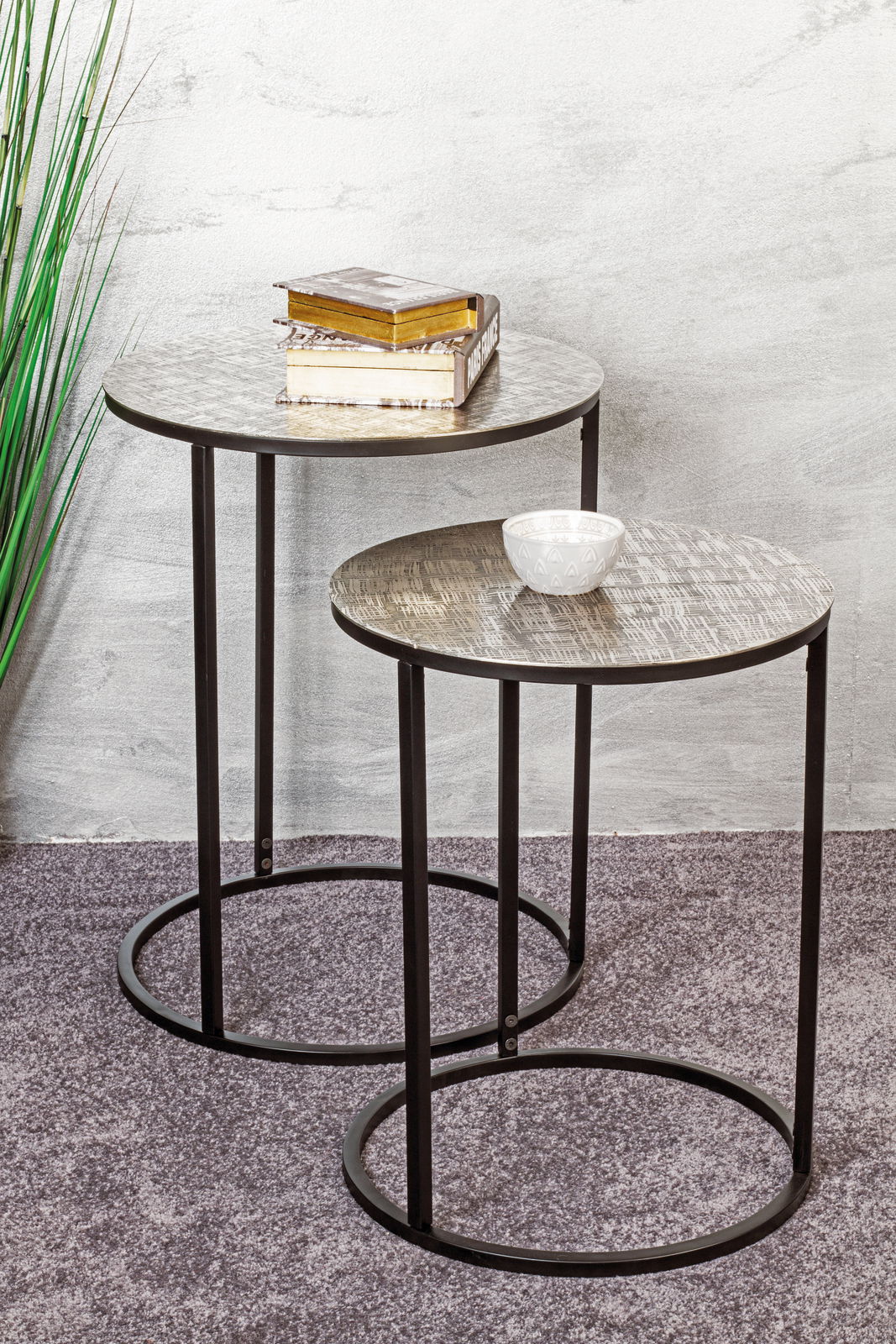 Zwei runde Beistelltische mit Metallgestell, einer mit Büchern und einer mit einer Schale, aus seitlicher Perspektive fotografiert.
