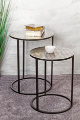 Zwei runde Beistelltische mit Metallgestell, einer mit Büchern und einer mit einer Schale, aus seitlicher Perspektive fotografiert.