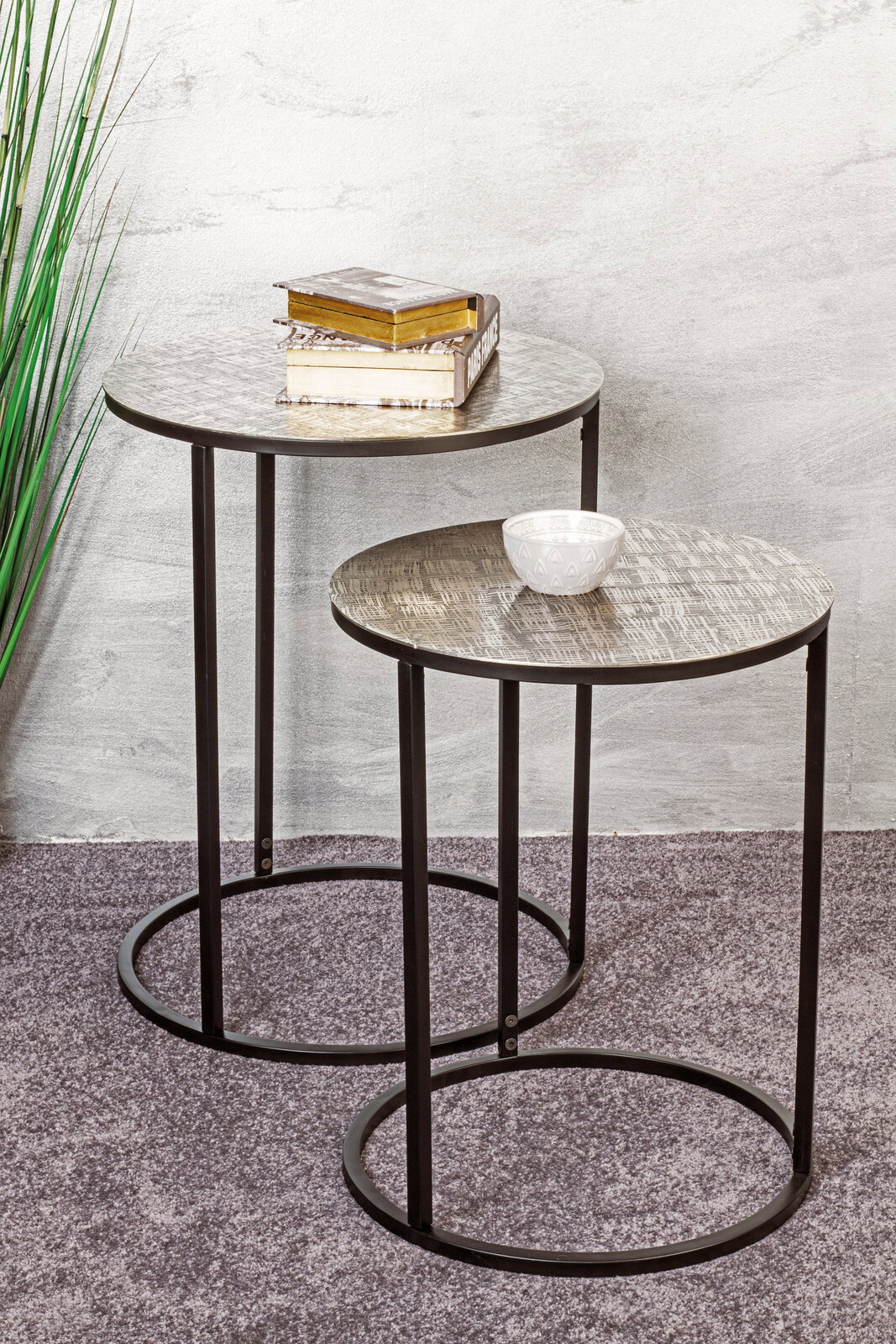Zwei runde Beistelltische mit Metallgestell, einer mit Büchern und einer mit einer Schale, aus seitlicher Perspektive fotografiert.
