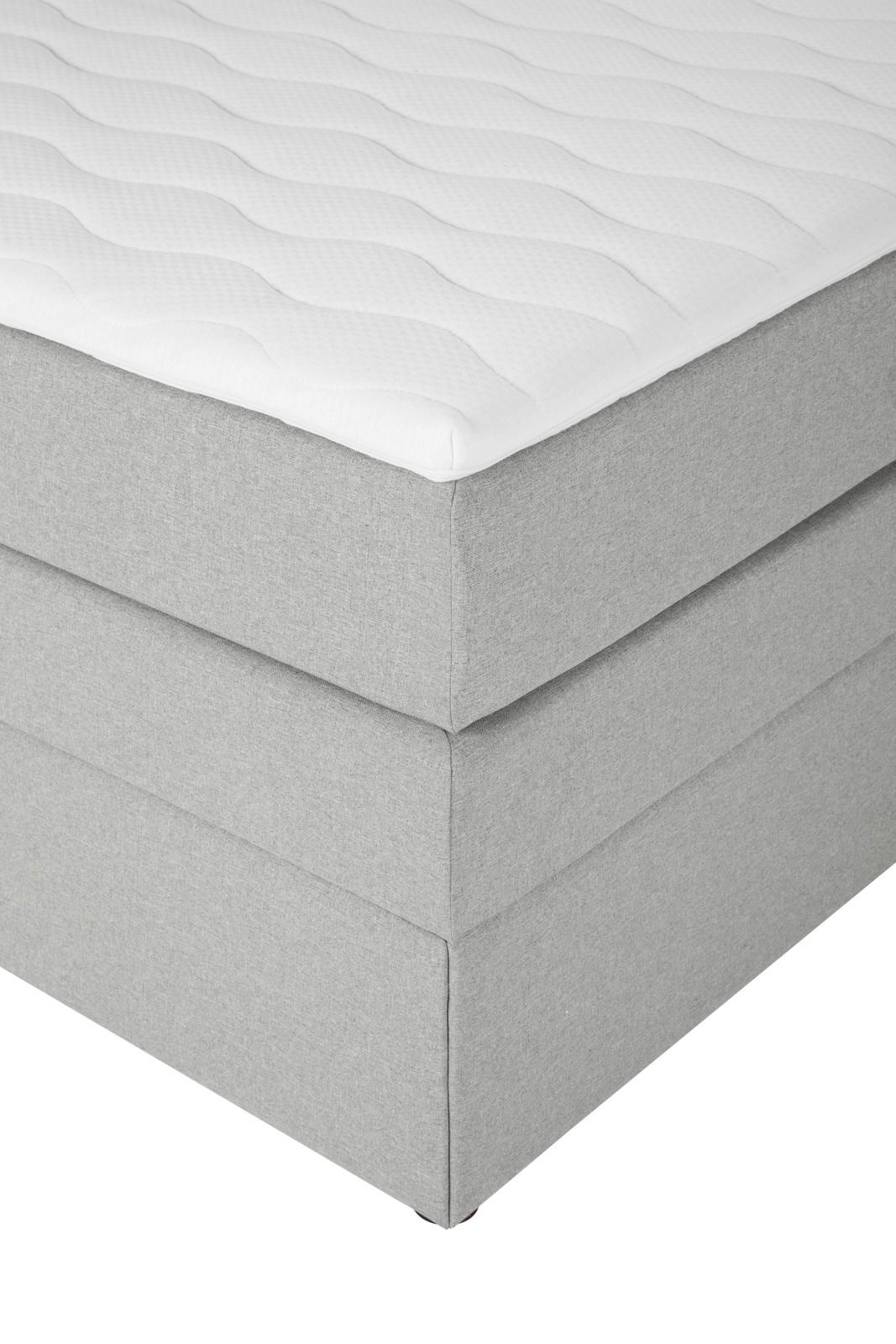 Ecke eines grauen Boxspringbetts mit weißem Topper, seitliche Perspektive