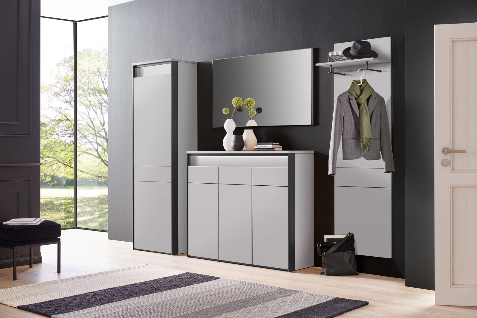 Voleo Garderoben-Set 4tlg. ZAYA Moderne Garderobeneinrichtung in einem hellen Raum mit großem Fenster, bestehend aus einem hohen Schrank, einer Kommode und einem Wandpaneel mit Kleiderhaken. Perspektive von vorne.