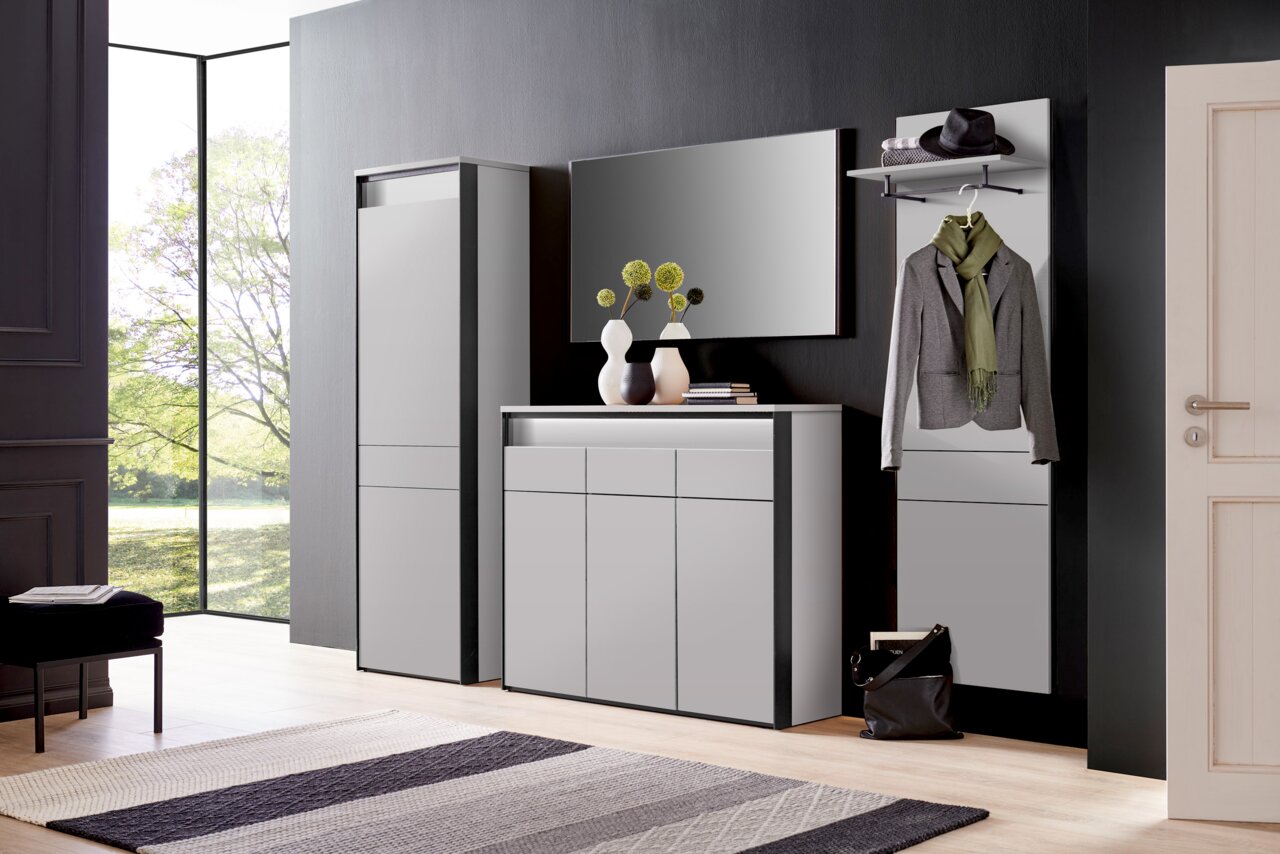 Voleo Sideboard ZAYA Moderne Garderobeneinrichtung in einem hellen Raum mit großem Fenster, bestehend aus einem hohen Schrank, einer Kommode und einem Wandpaneel mit Kleiderhaken. Perspektive von vorne.