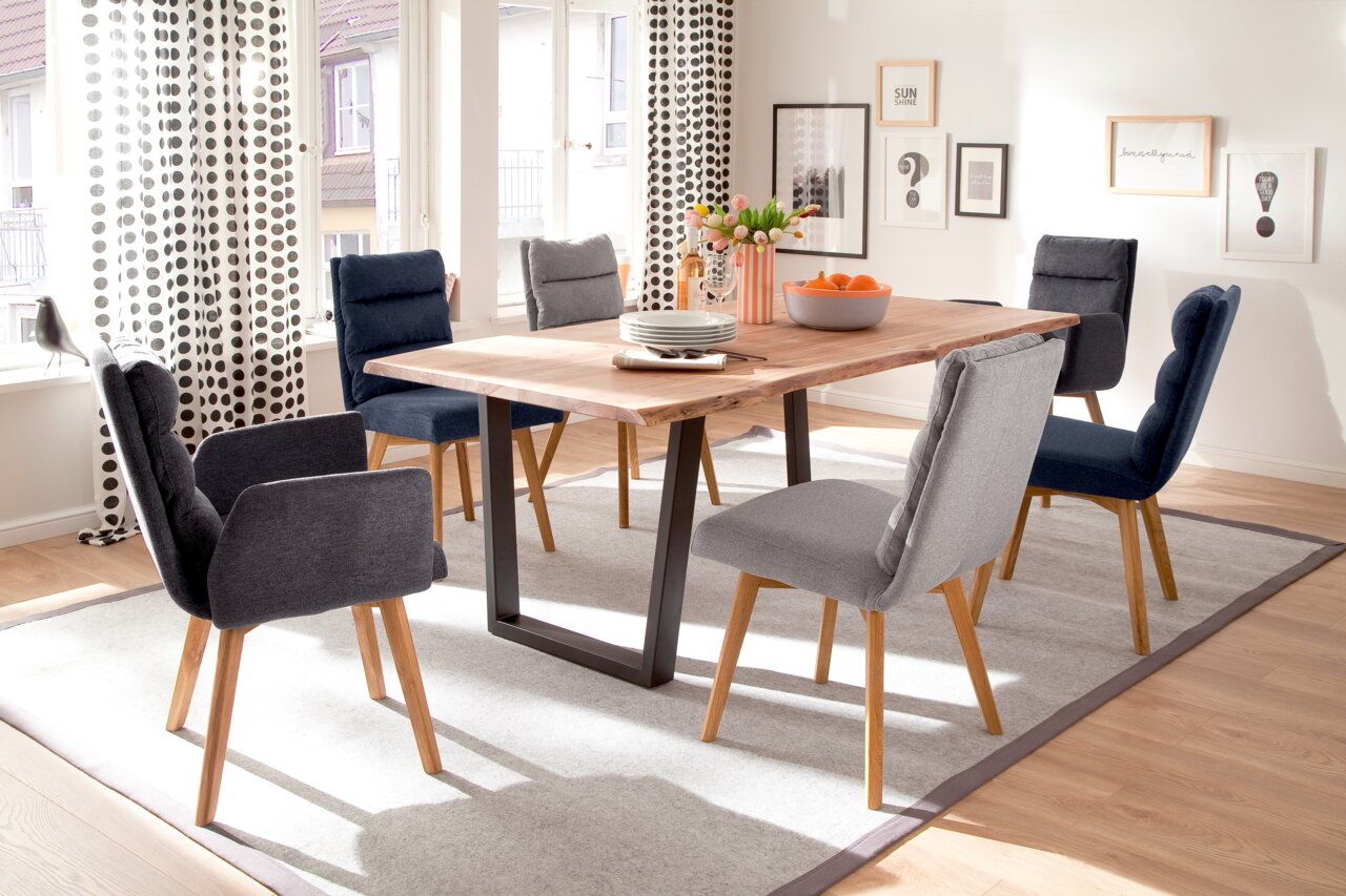 Moderner Esstisch mit Holzplatte und schwarzen Metallbeinen, umgeben von gepolsterten Stühlen in einem hellen Esszimmer. Perspektive von der Seite.