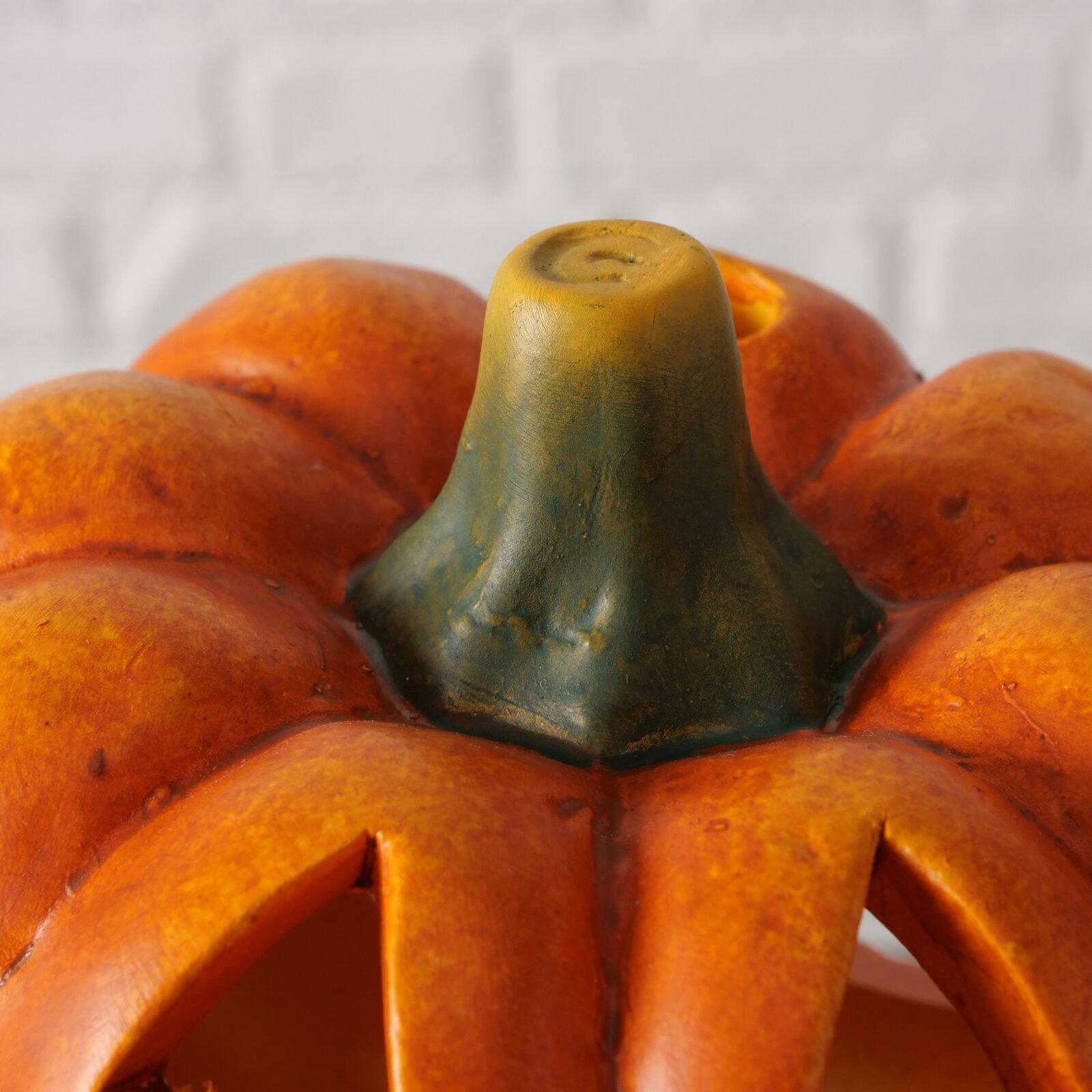 Close-up van een theelichthouder in de vorm van een pompoen met een oranje oppervlak en een groene steel, gezien van bovenaf.