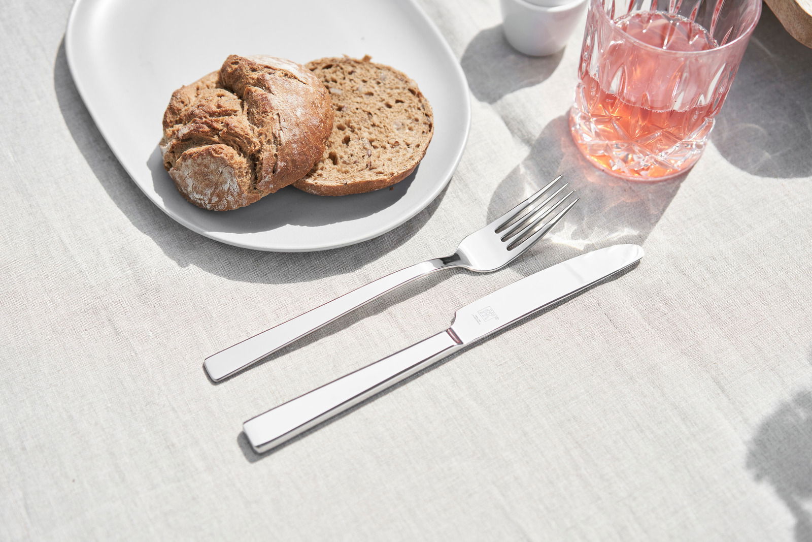 Elegantes Besteckset bestehend aus Messer und Gabel auf einem gedeckten Tisch mit Brot und Getränk, aus der Vogelperspektive fotografiert.