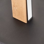 Detailaufnahme aus schräger Seitenperspektive eines Standfußes aus naturbelassenem Holz mit silberfarbenem Metallprofil auf dunkler Oberfläche