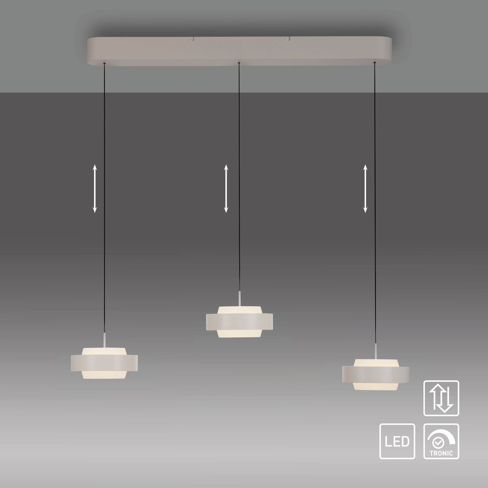 Moderne LED-hanglamp met drie lampen in wit, met een langwerpige kap en in hoogte verstelbare kabels; vooraanzicht, licht van onderaf gefotografeerd tegen een grijze achtergrond
