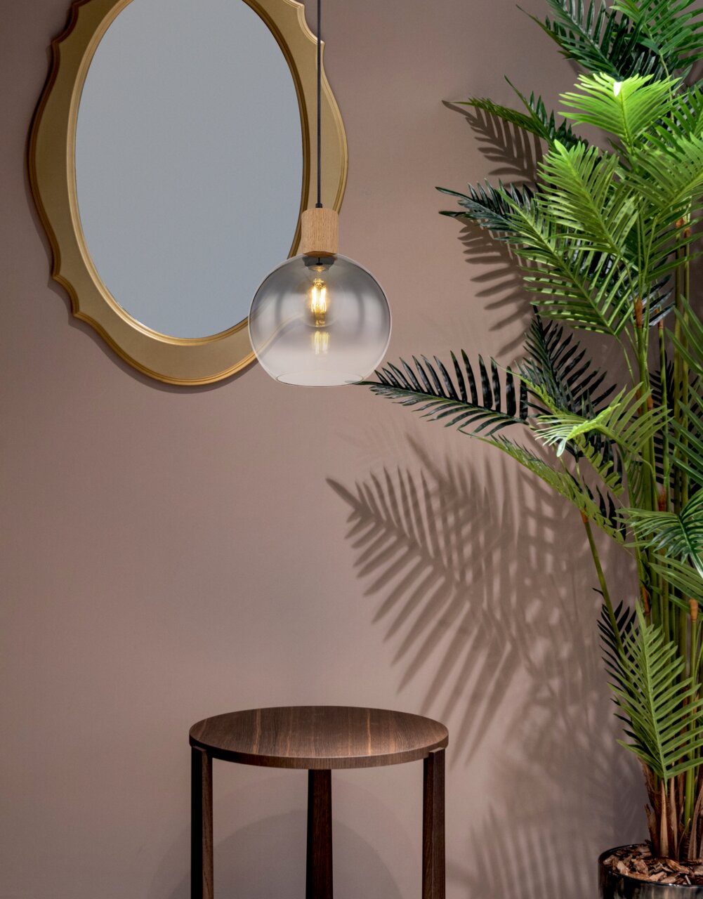 Hängeleuchte mit rundem, transparentem Glasschirm und Holzdetail, von der Seite betrachtet, neben einem runden Spiegel und einer Pflanze.