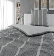 Grau-weiß gestreifte Bettwäsche mit passendem Kissen auf einem weißen Bett im modernen Schlafzimmer, aufgenommen in leichter Schrägansicht von vorn/oben.