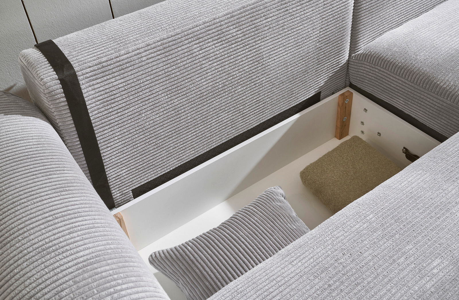 Nahaufnahme einer grauen Eckcouch mit Stauraum, geöffnet, mit Kissen und Decke. Perspektive von oben.