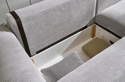 Nahaufnahme einer grauen Eckcouch mit Stauraum, geöffnet, mit Kissen und Decke. Perspektive von oben.
