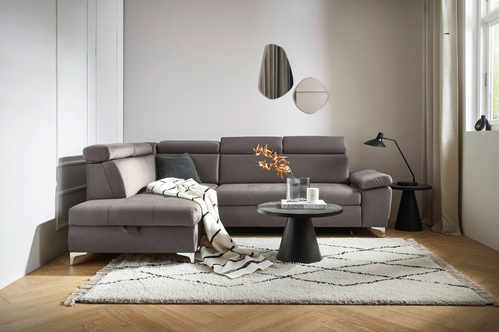 Graue Rundecke (L) in einem modernen Wohnzimmer, mit einem Beistelltisch und Dekorationen, aus der Perspektive von vorne links.