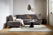 Graue Rundecke (L) in einem modernen Wohnzimmer, mit einem Beistelltisch und Dekorationen, aus der Perspektive von vorne links.