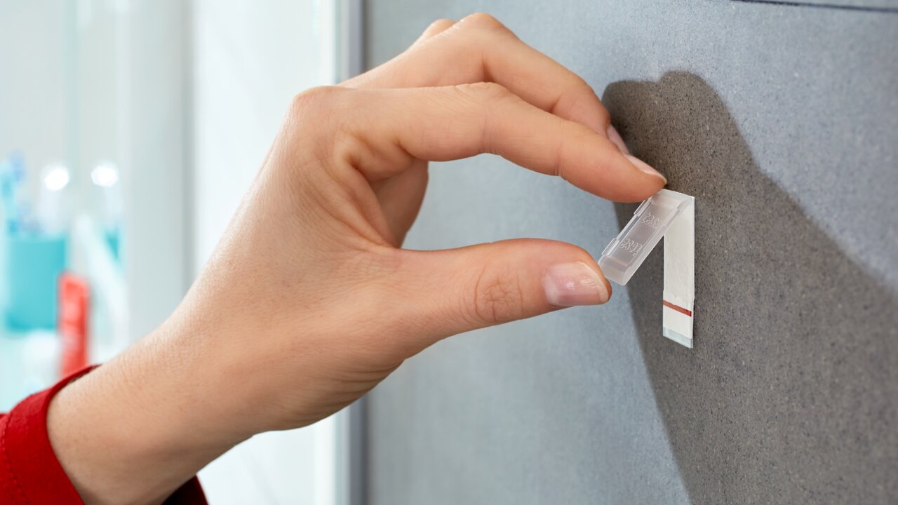 Nahaufnahme einer Hand, die einen tesa Powerstrip Waterproof an einer Wand anbringt.