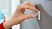 Nahaufnahme einer Hand, die einen tesa Powerstrip Waterproof an einer Wand anbringt.