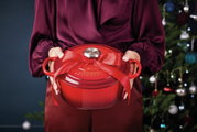 Roter runder Bräter mit Schleife, von vorne gehalten, vor einem Weihnachtsbaum