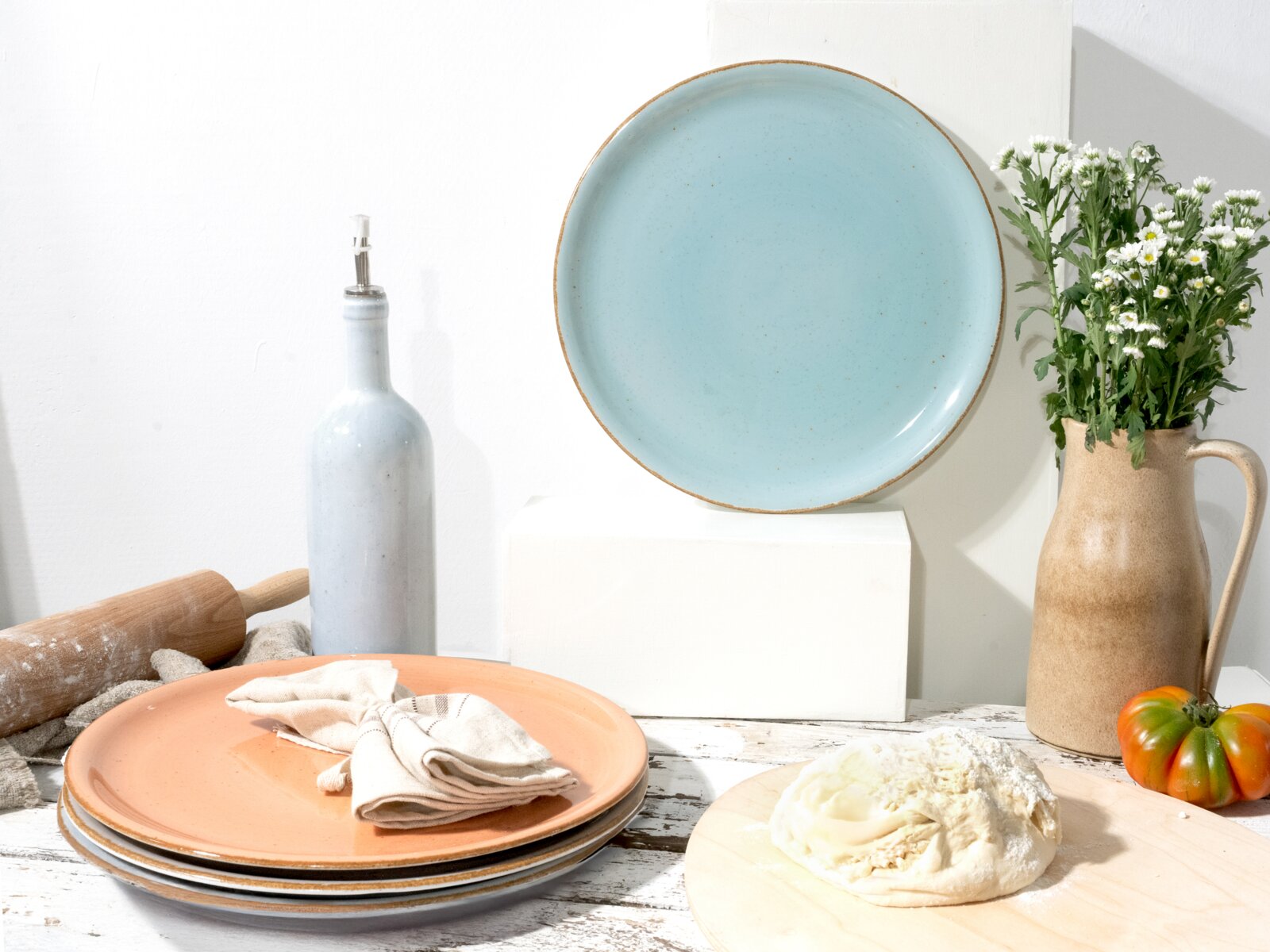 Creatable Pizzateller 4-tlg VINTAGE NATURE Hellblauer Keramikteller mit braunem Rand, frontal in leichter Aufsicht vor weißem Hintergrund, umgeben von weiteren Tellern, Ölflasche, Nudelholz, Krug mit Blumen und Teig auf Holzbrett.