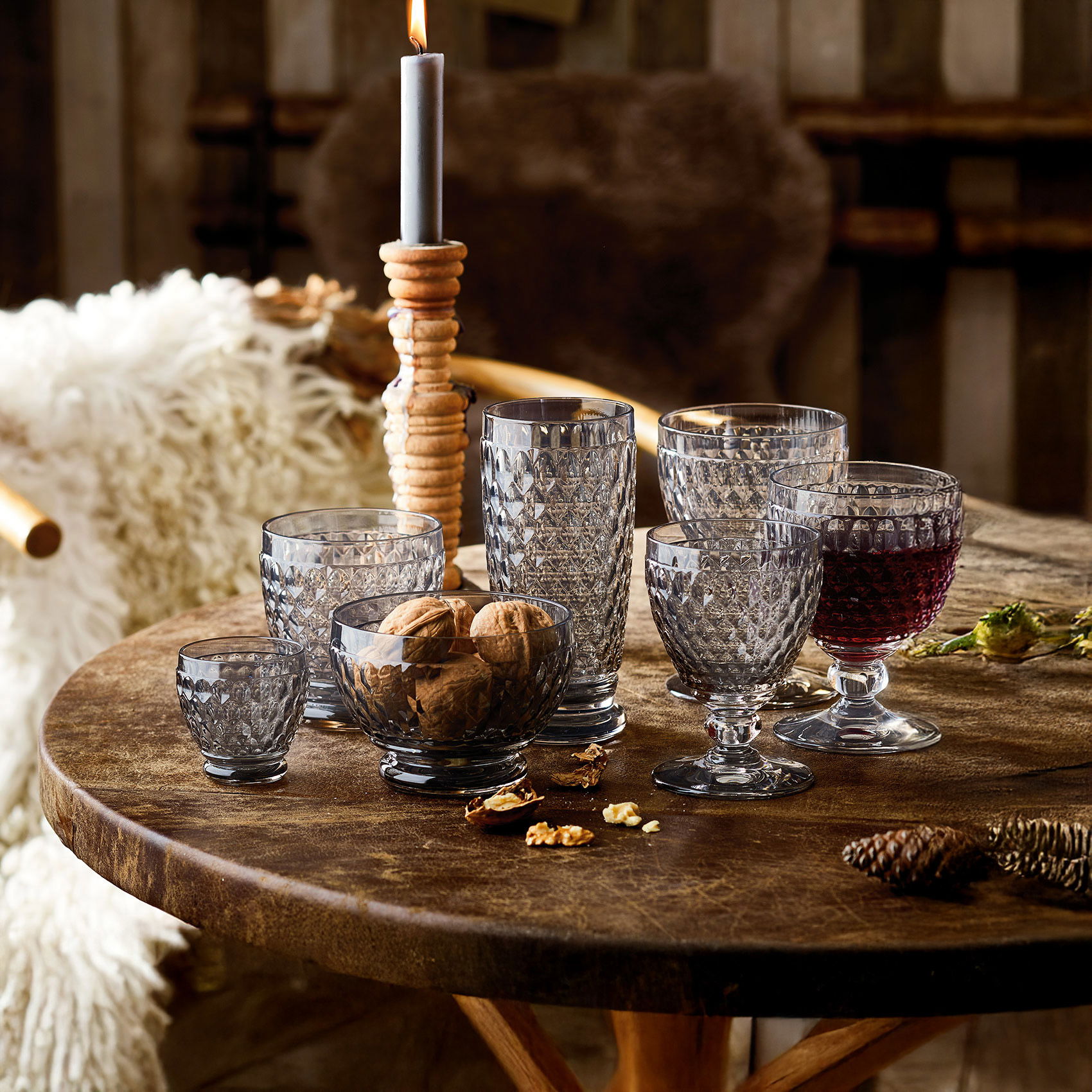 Rustikaler Holztisch mit dekorativen, facettierten Trinkgläsern, Nüssen und einer brennenden Kerze in gemütlicher Atmosphäre