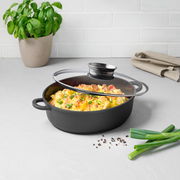 Alugussbräter mit Glasdeckel, gefüllt mit überbackenem Gericht, auf einer Küchenarbeitsplatte, seitliche Perspektive