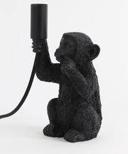 Schwarze Tischleuchte in Form eines Affen, der eine Lampenfassung in der Hand hält. Seitliche Perspektive.