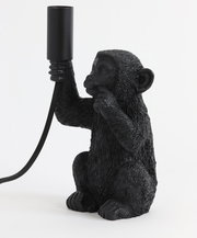 Schwarze Tischleuchte in Form eines Affen, der eine Lampenfassung in der Hand hält. Seitliche Perspektive.