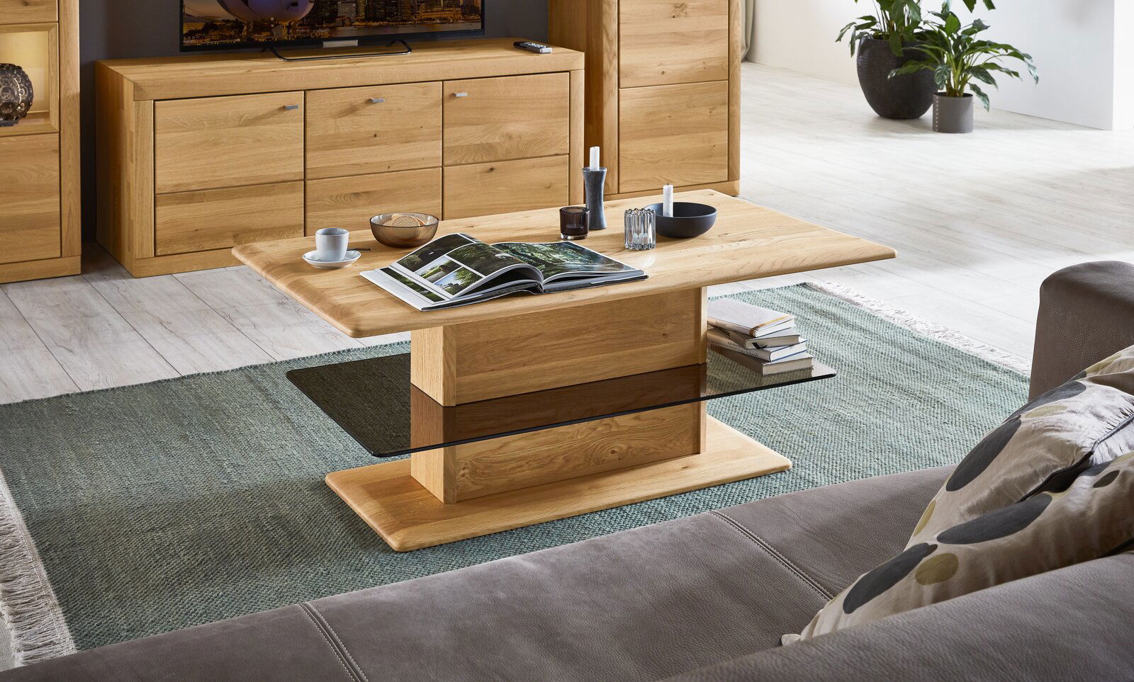 Moderner Couchtisch aus Holz mit rechteckiger Tischplatte und stabiler Mittelsäule, umgeben von gemütlichem Wohnzimmerambiente. Perspektive von schräg oben.