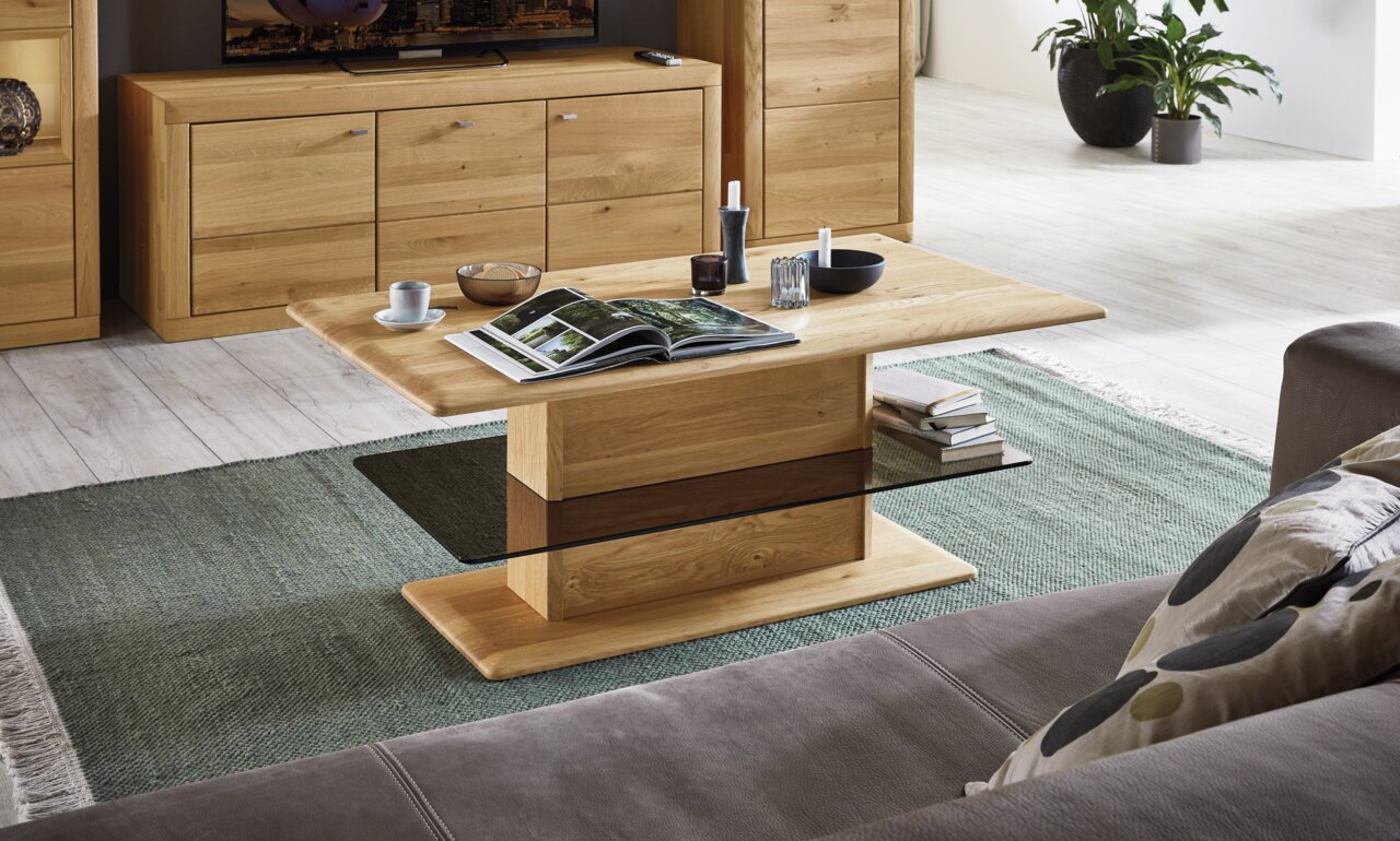 Moderner Couchtisch aus Holz mit rechteckiger Tischplatte und stabiler Mittelsäule, umgeben von gemütlichem Wohnzimmerambiente. Perspektive von schräg oben.