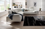 Moderne Polsterrundecke in einem hellen Wohnzimmer mit großen Fenstern, dekorativen Kissen und einem eleganten Couchtisch. Perspektive von vorne links.