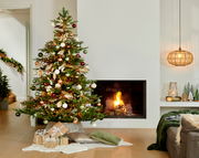 Weihnachtsbaum mit bunten Kugeln und Lichtern, neben einem brennenden Kamin, aus der Perspektive des Wohnzimmers.