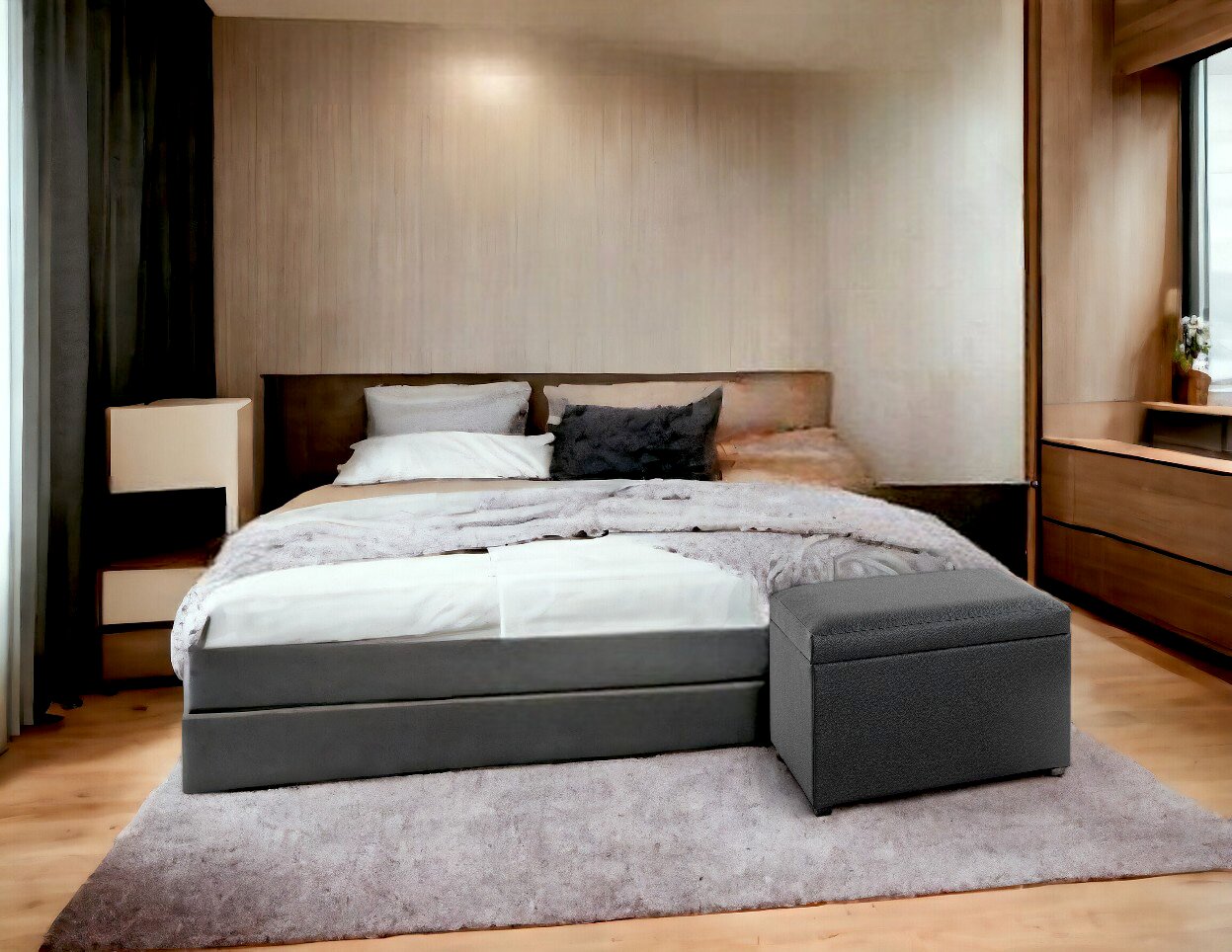 Modernes Schlafzimmer mit grauem Polsterbett, weißen Kissen und Tagesdecke sowie gepolstertem Hocker am Fußende, frontal aus leicht erhöhter Perspektive aufgenommen.