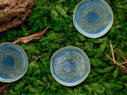 Drei runde Keramik-Teller in Blau- und Grüntönen mit reaktiver Glasur auf grünem Moos mit Holzstücken, Draufsicht von oben