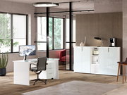 Moderner Büroraum mit weißem Schreibtisch, Bürostuhl und niedrigem Aktenschrank, seitliche Perspektive