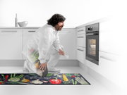 Küchenläufer mit buntem Gemüse-Design und der Aufschrift 'Natural Food', in einer modernen weißen Küche vor einem Backofen platziert. Perspektive von der Seite.